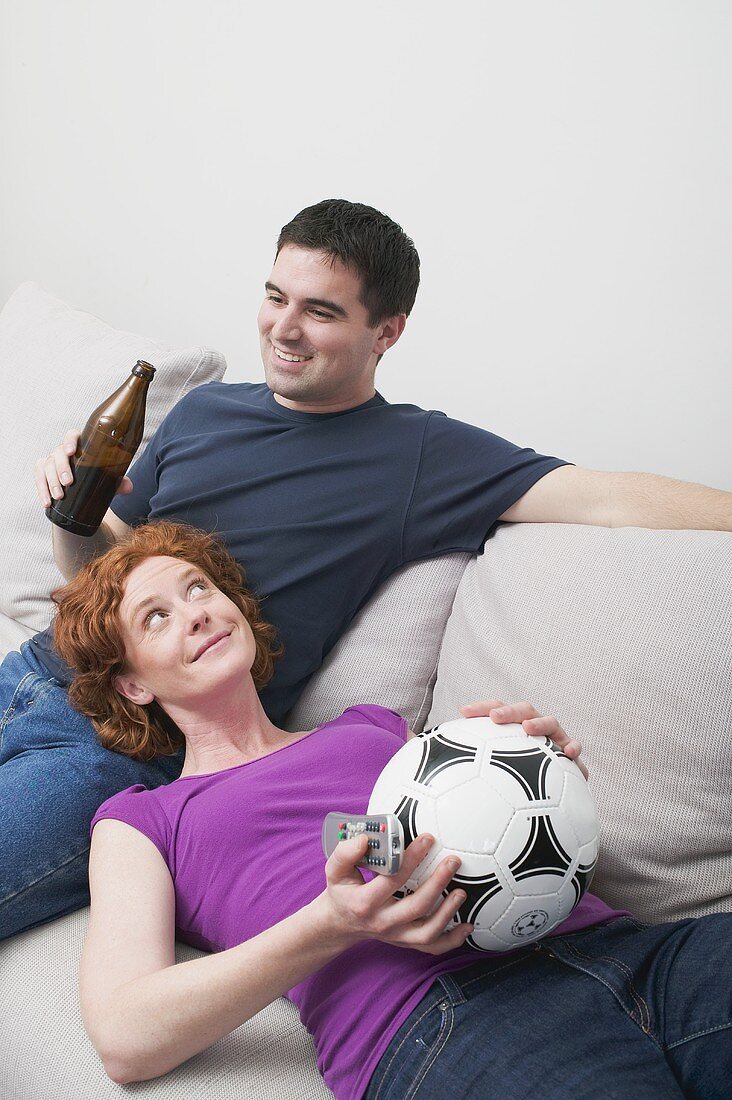 Junges Paar mit Fussball und Bierflasche auf dem Sofa