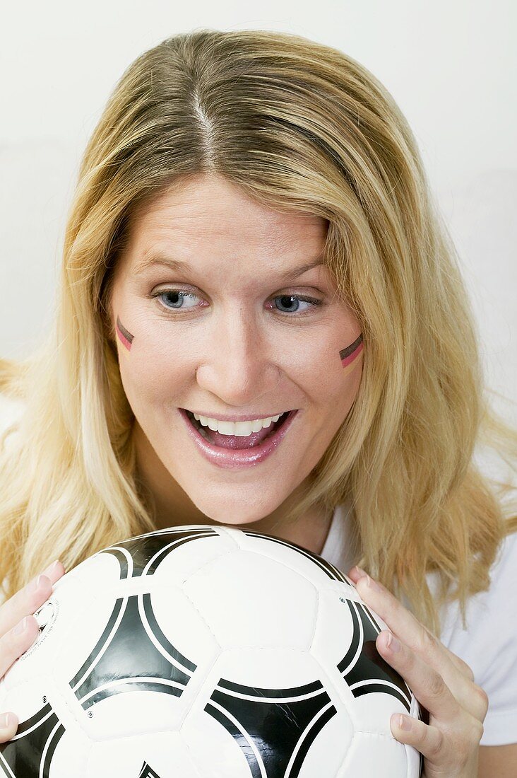 Young woman with German colours on her face holding football