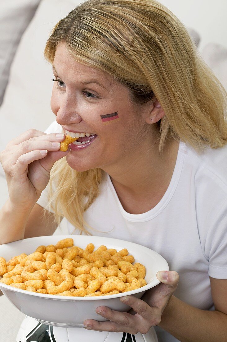 Junge Frau mit Deutschland-Farben im Gesicht isst Chips