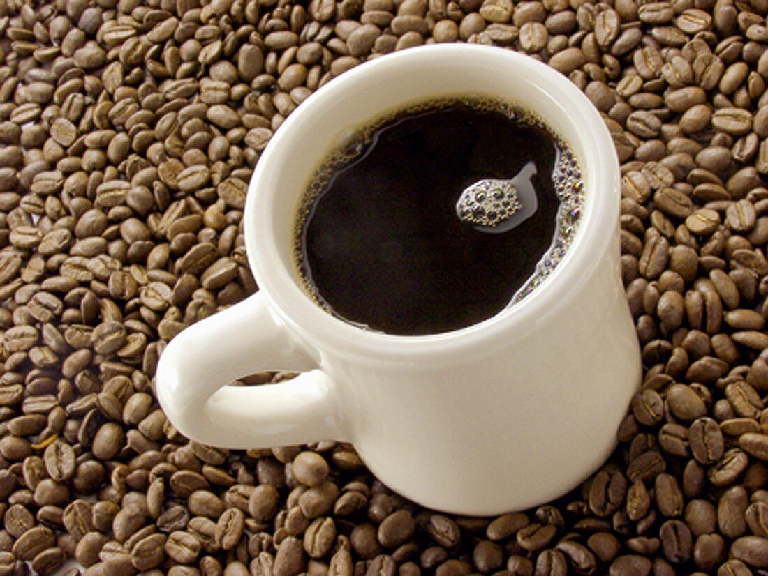 Mug of Black Coffee Resting on Coffee Beans