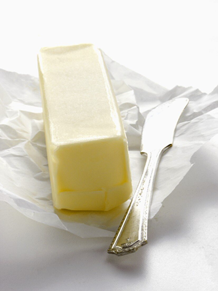Stück Butter auf Einwickelpapier mit Buttermesser