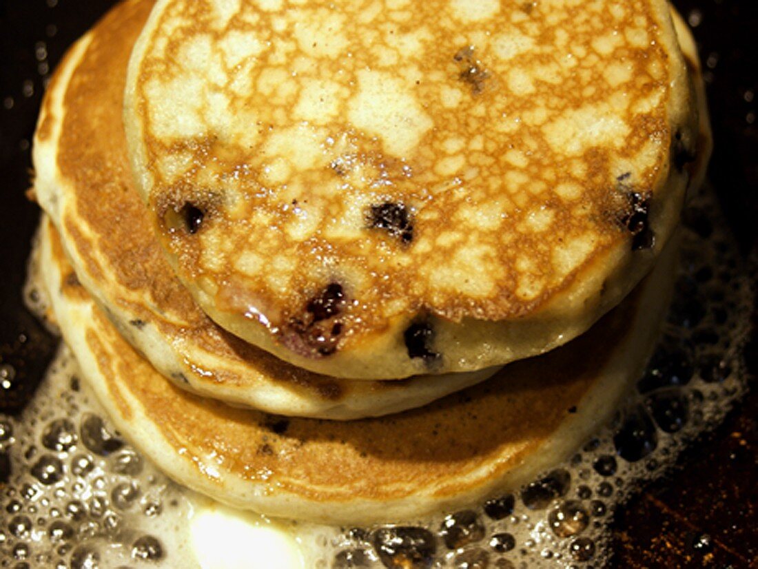 Three Blueberry Pancakes Cooking on a Grill with Butter