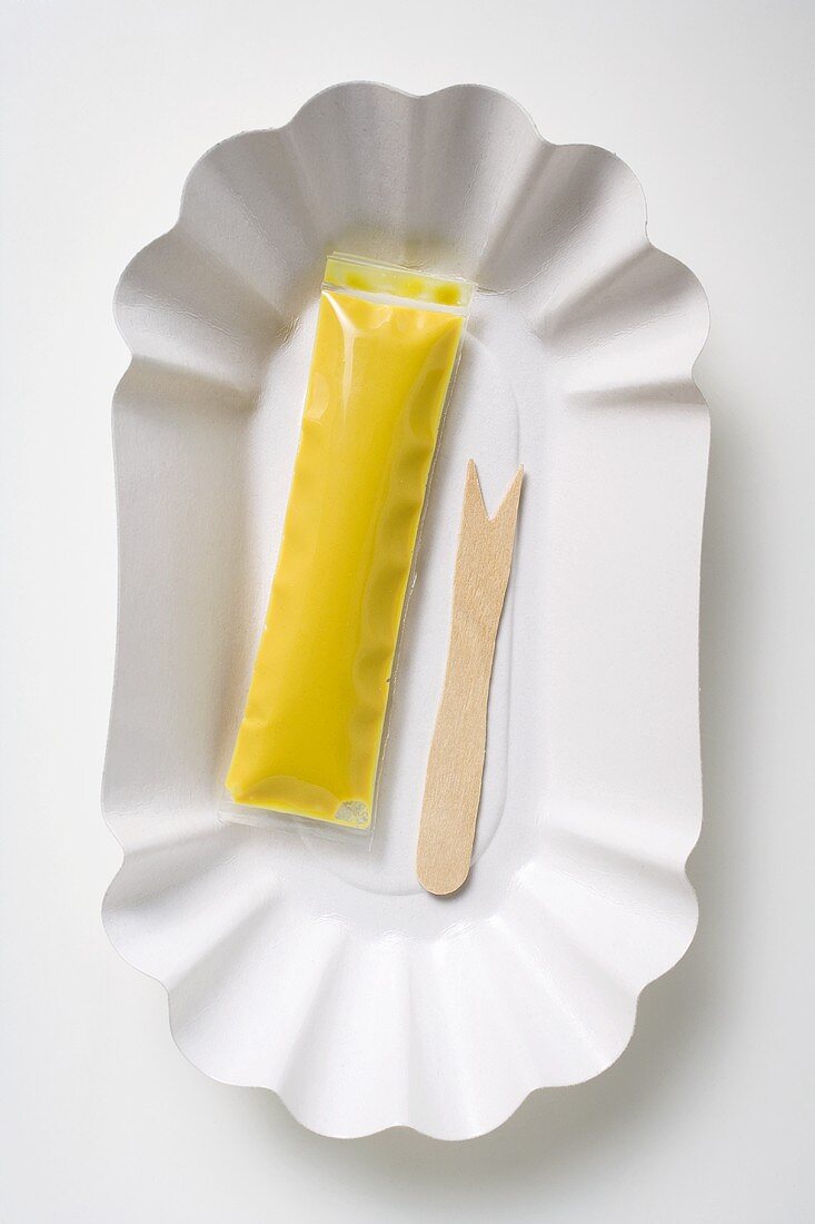 Wooden fork and sachet of mustard on paper plate