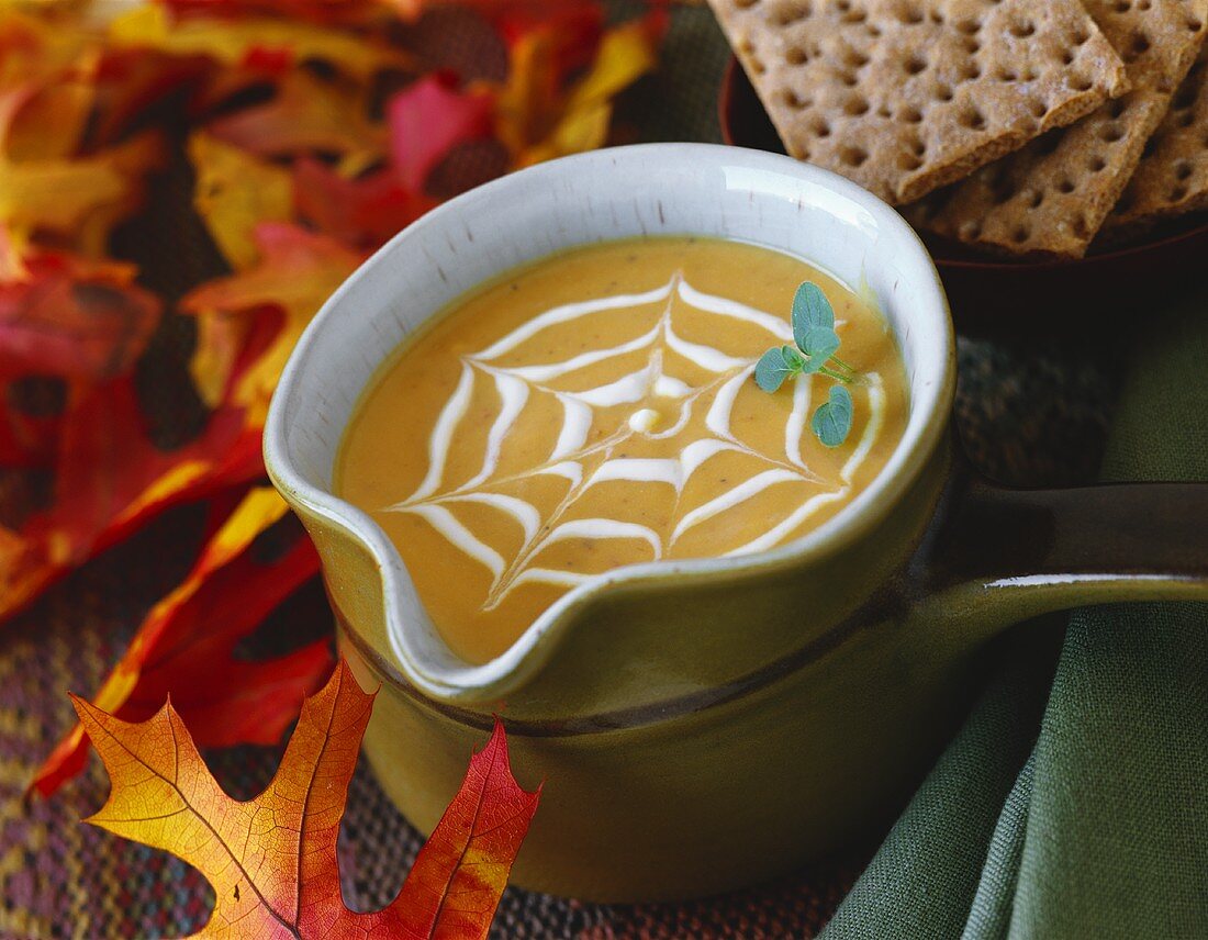 Cream of pumpkin soup with cobweb pattern & autumn leaves