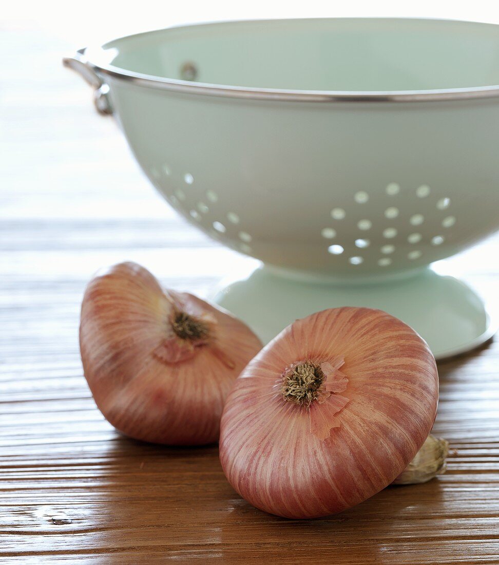 Two Red Onions with a Colander on Wood Surface