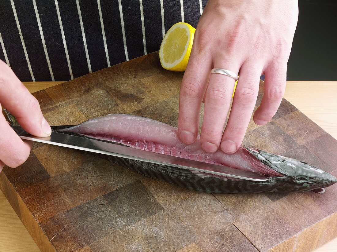 Man Slicing Mackerel with Knife on Cutting Board