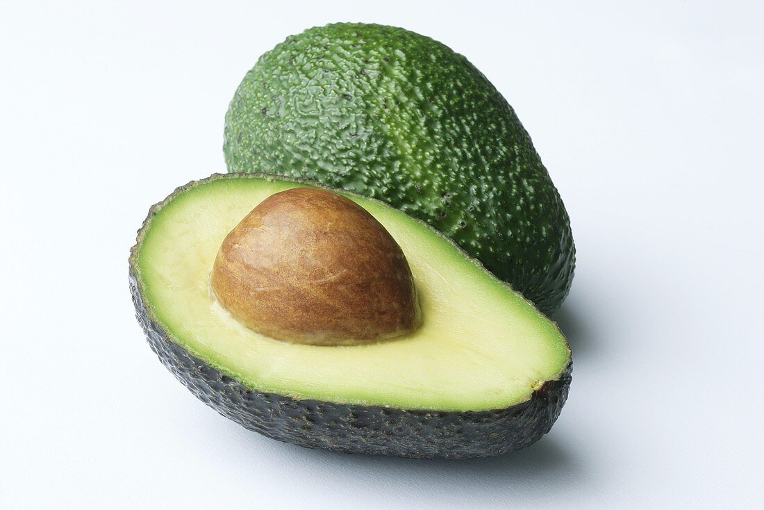 Half an avocado with stone and a whole avocado