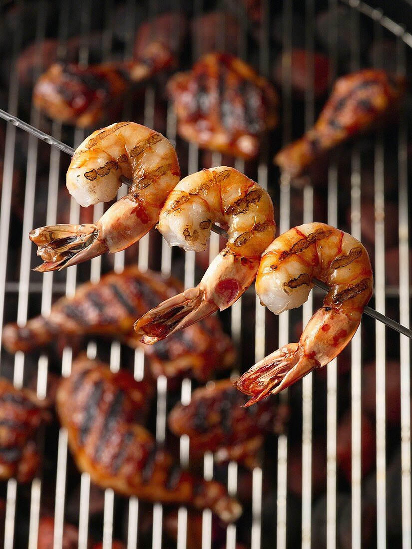 Gegrillter Garnelenspiess mit Hähnchenteilen im Hintergrund