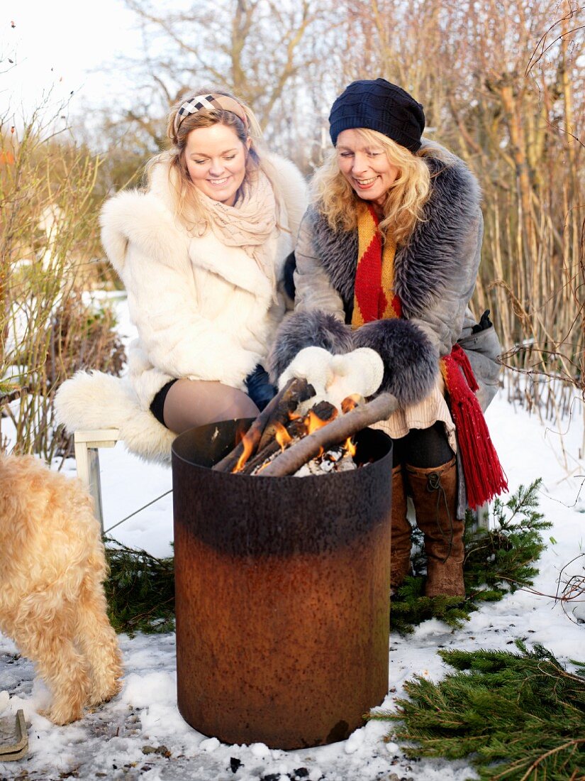 Zwei Frauen am Holzfeuer im winterlichen Garten