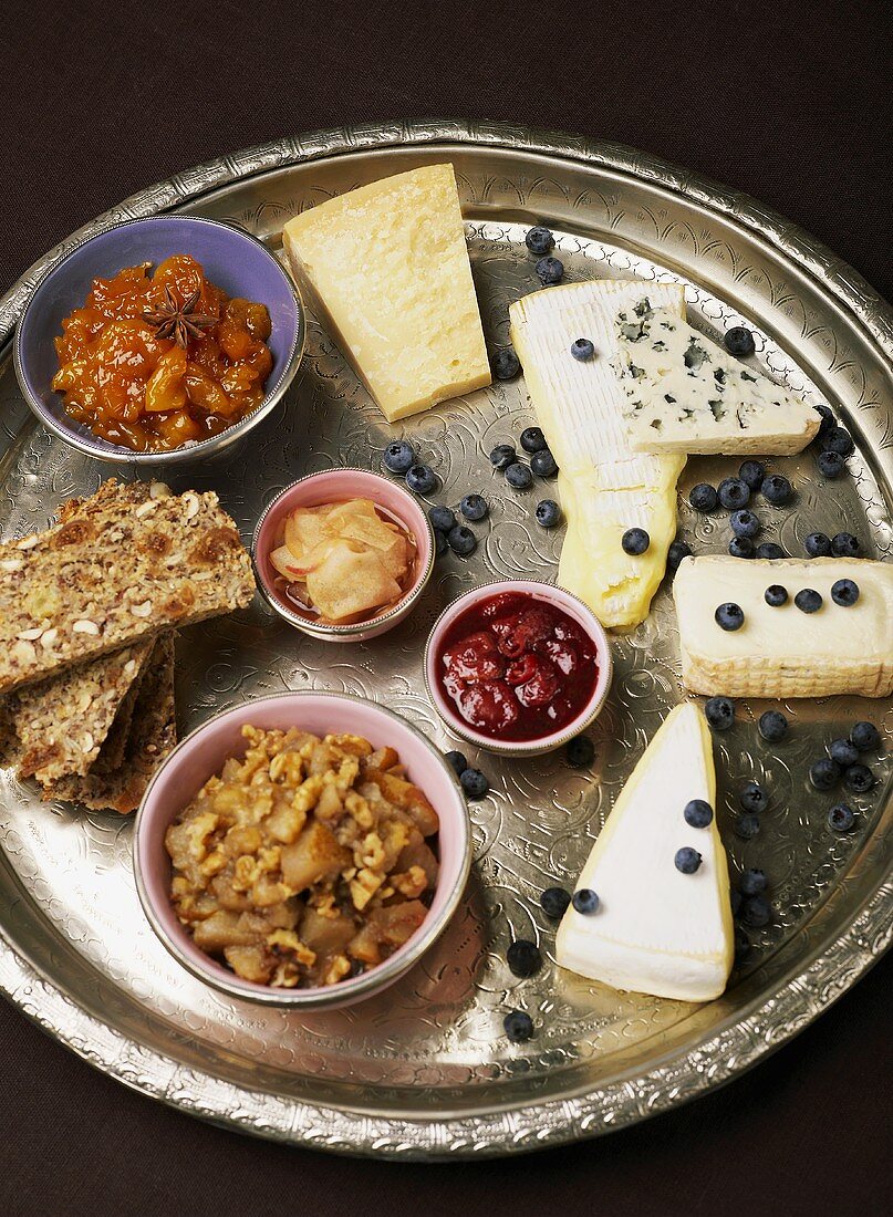 A cheese platter with bread, chutney and lingonberries