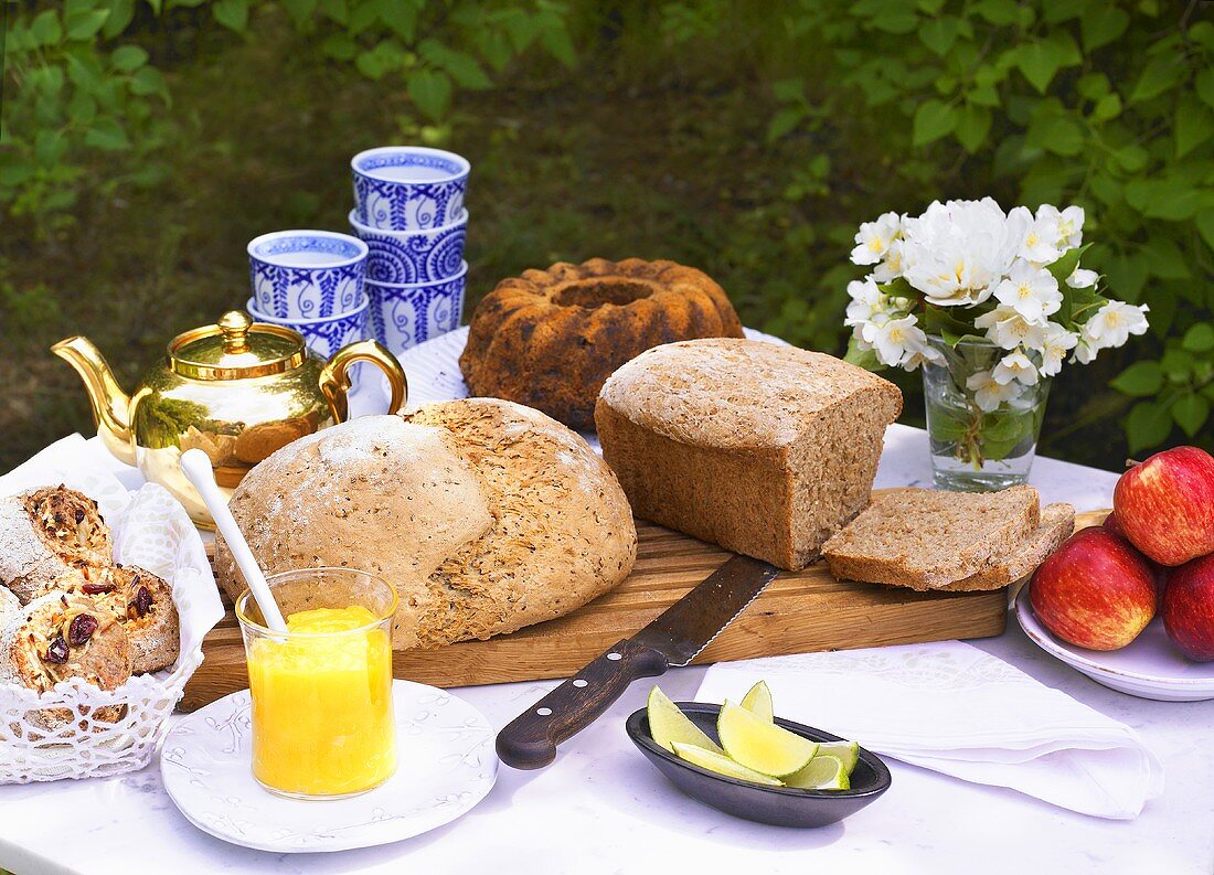 A garden table laid with bread, cake, tea and fruit