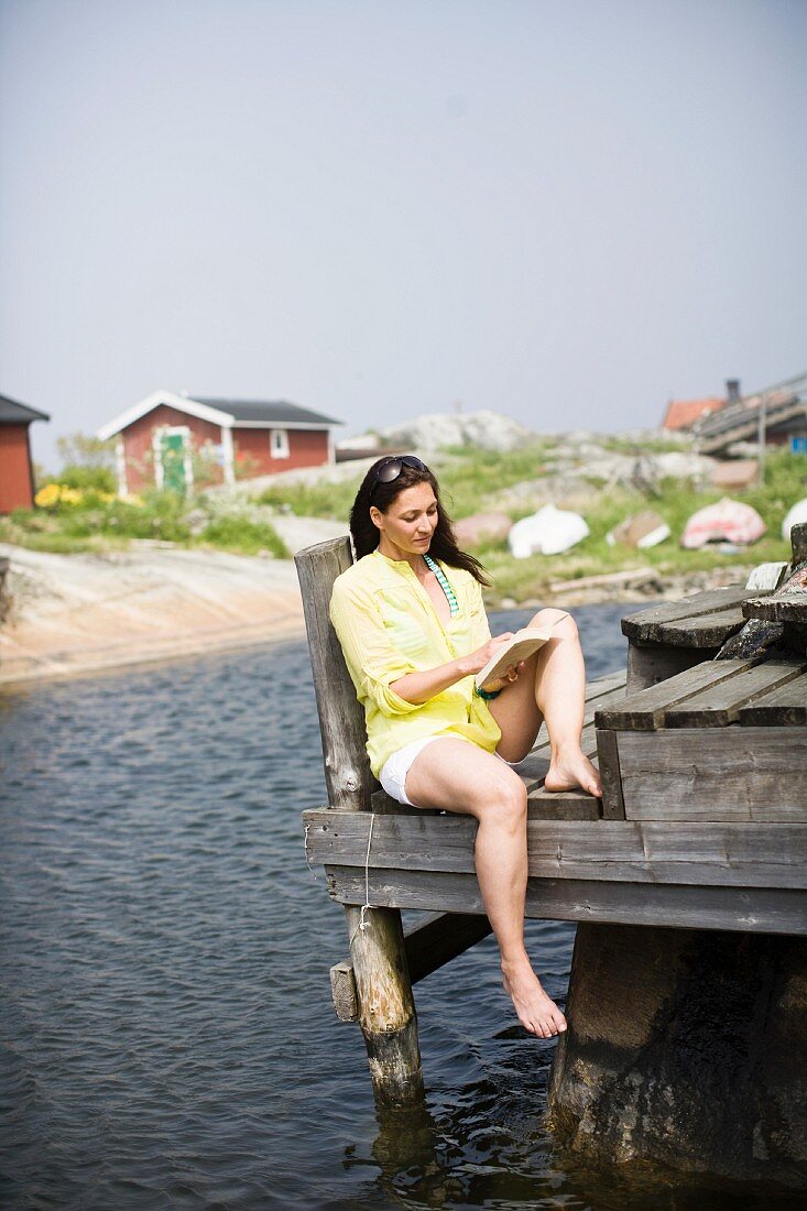 Frau liest ein Buch auf Anlegesteg am Meer