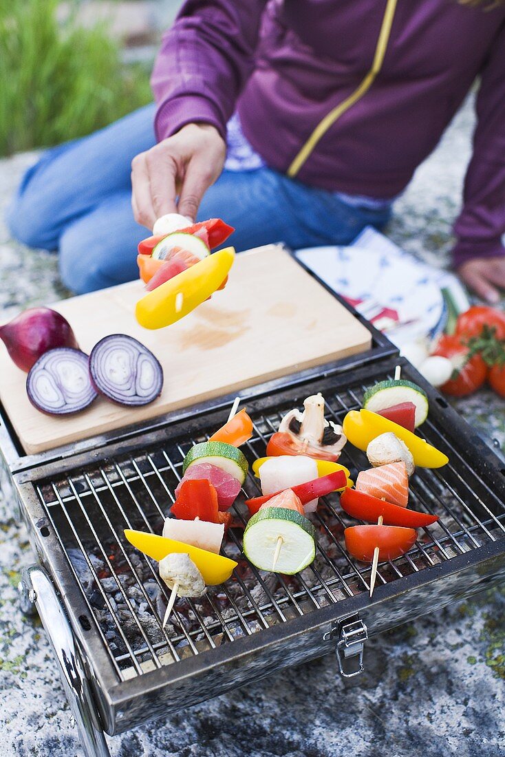 Person grillt Spiesse am Strand