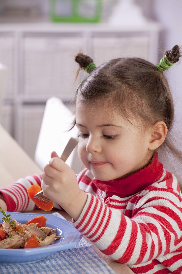 A little girl eating chicken and carrots