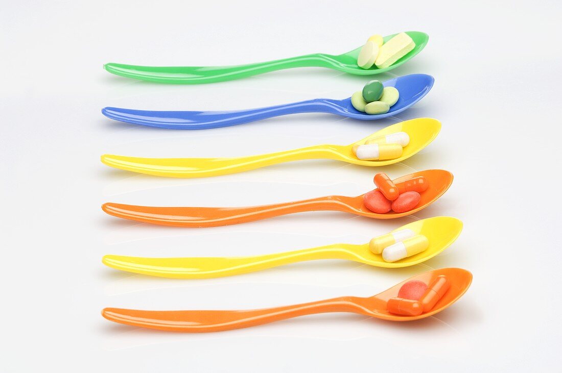 A row of spoons with vitamin tablets
