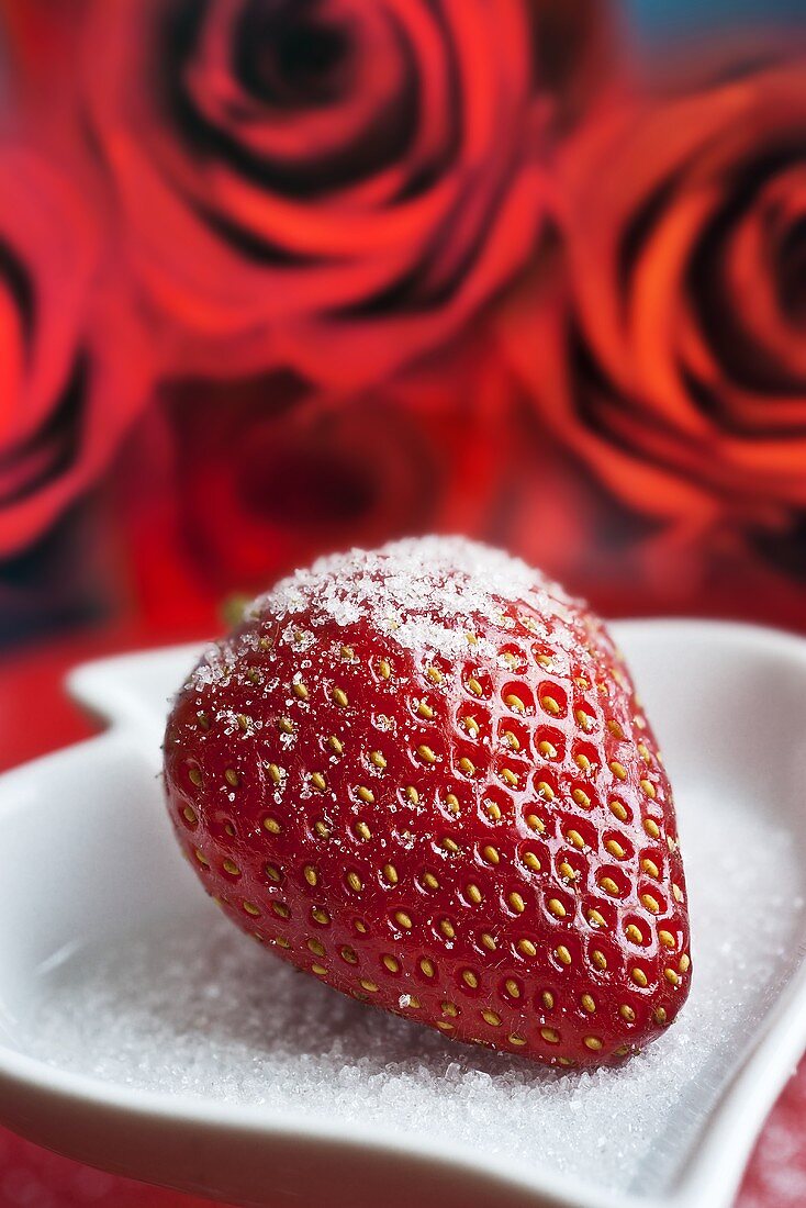 A sugared strawberry with roses in the background
