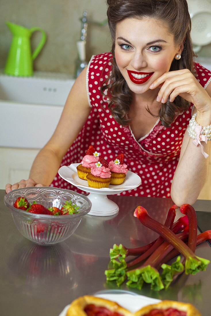 Mädchen im Retro-Look mit Erdbeermuffins, Erdbeeren und Rhabarber