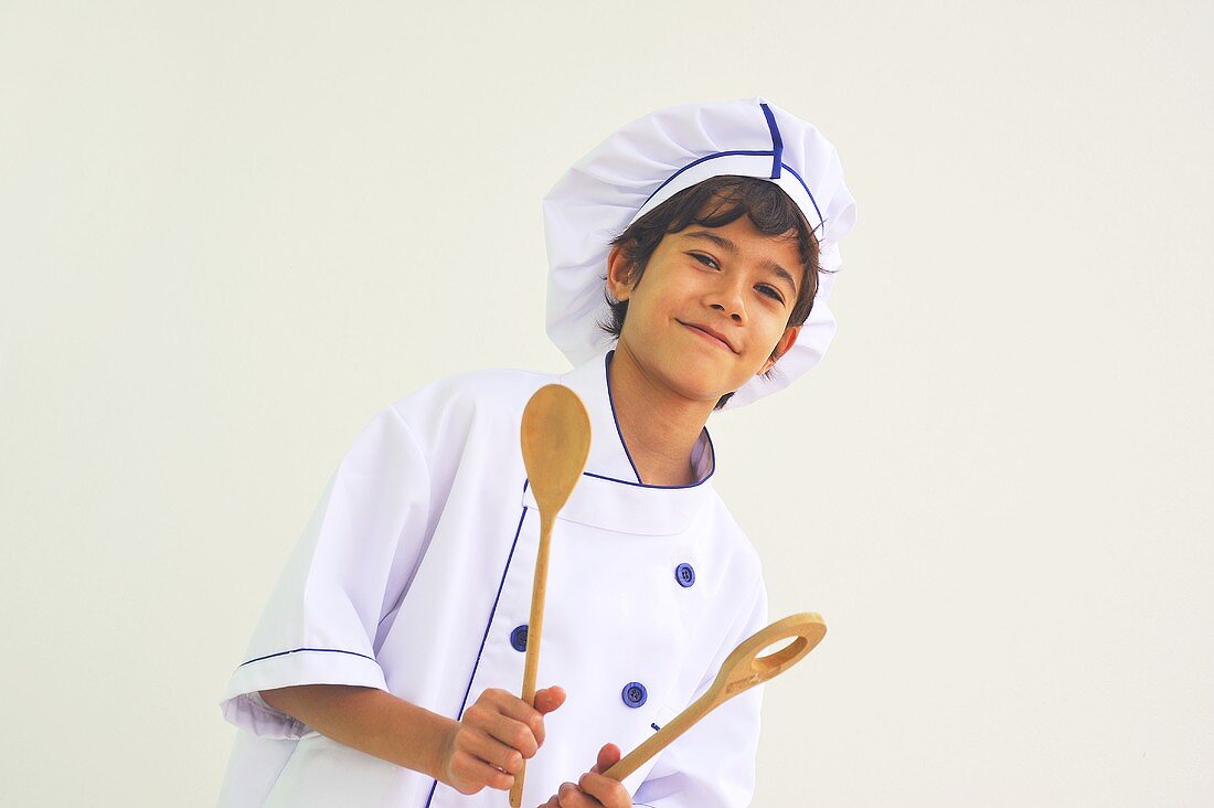 A boy dressed as a chef holding wooden spoons