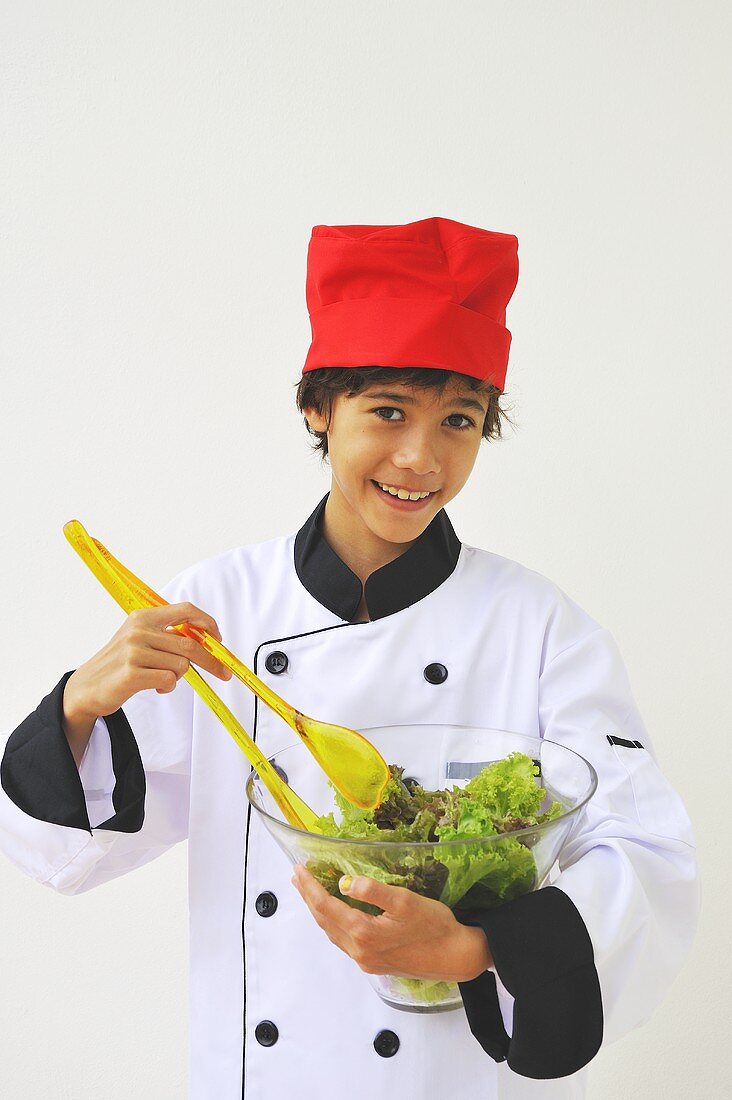 A boy dressed as a chef mixing salad