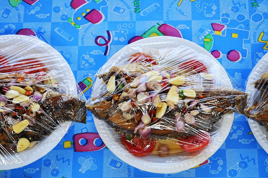 Sweet-sour tilapia on plates covered with clingfilm
