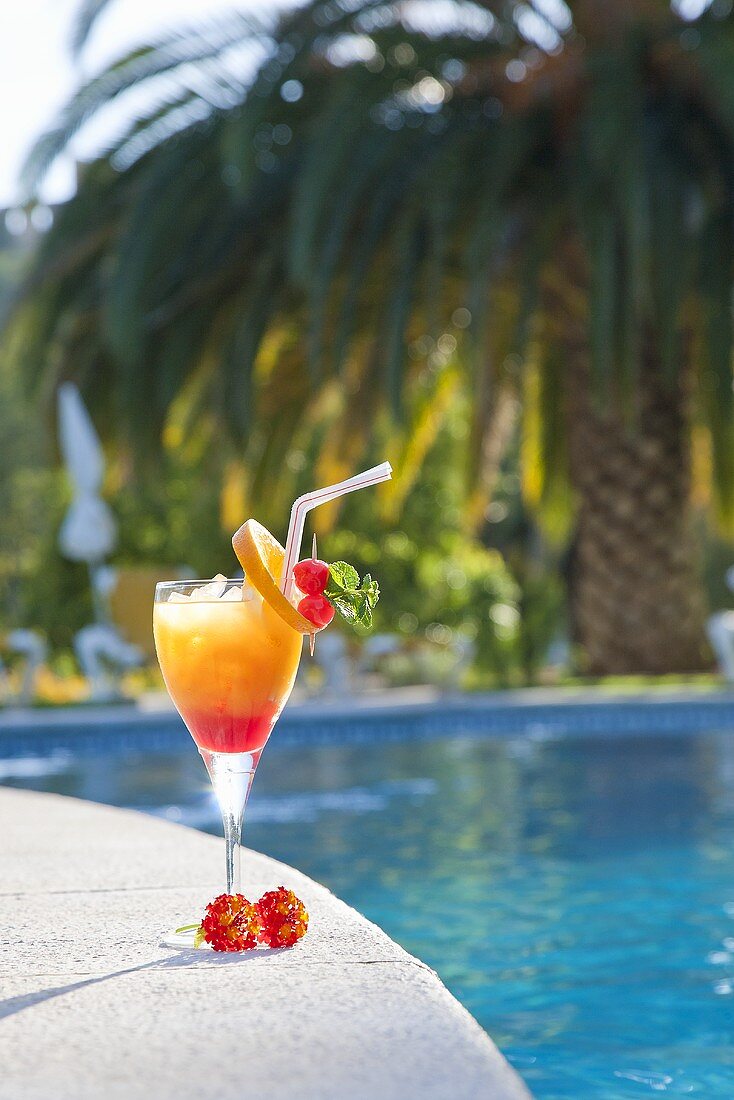 Ein Glas Tequila Sunrise am Swimming Pool, im Hintergrund eine Palme