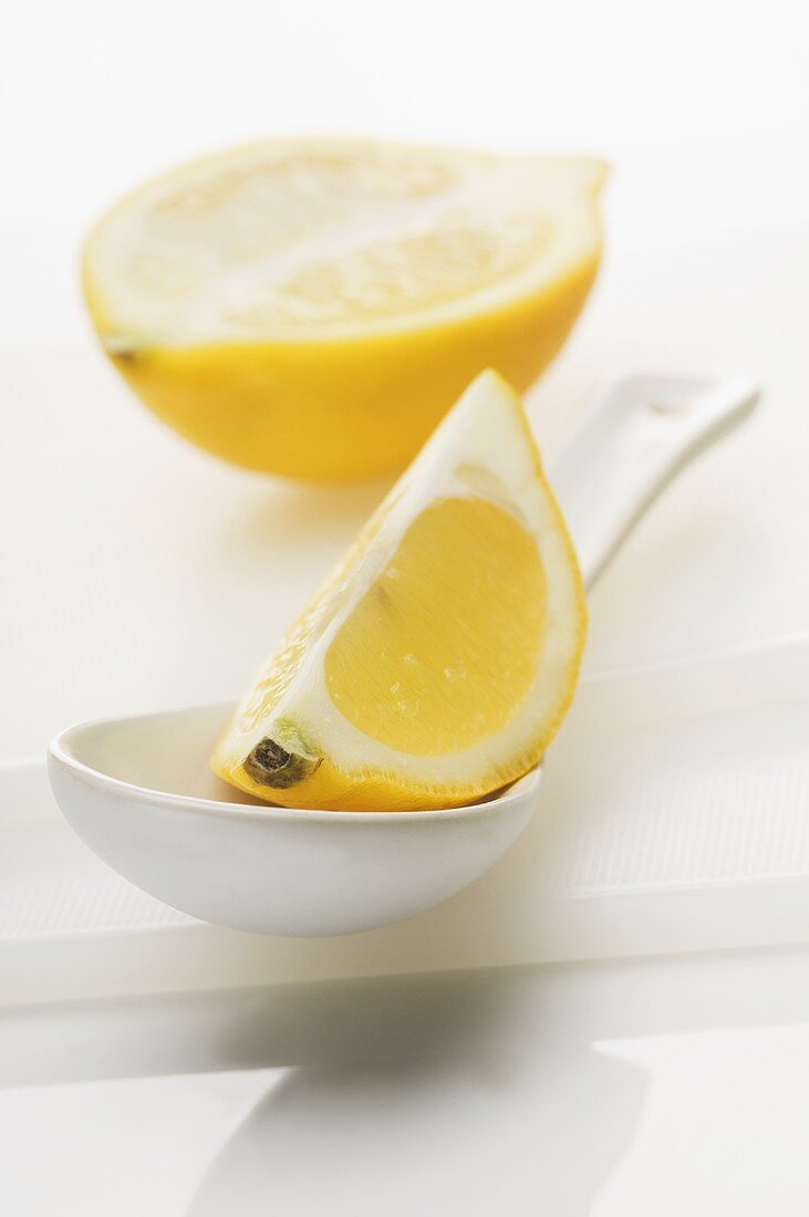 A lemon wedge on a spoon with half a lemon in the background