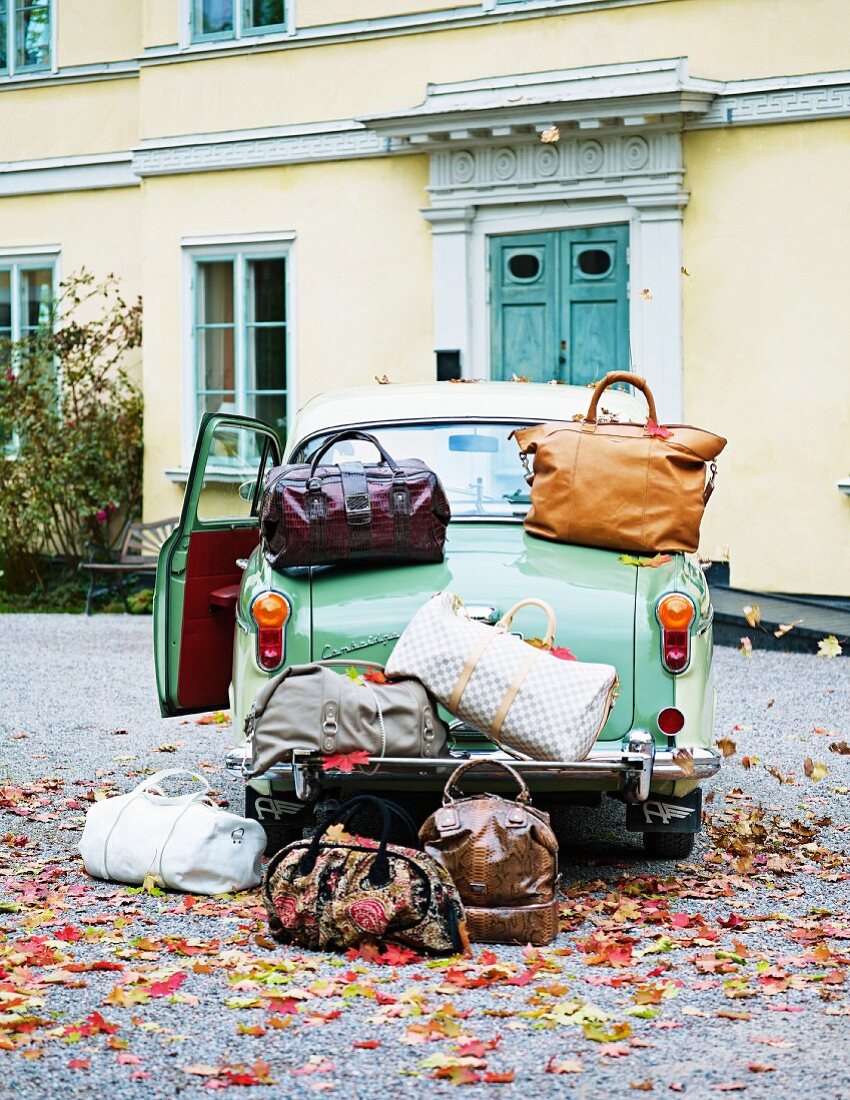 A classic car and lots of luggage outside a house
