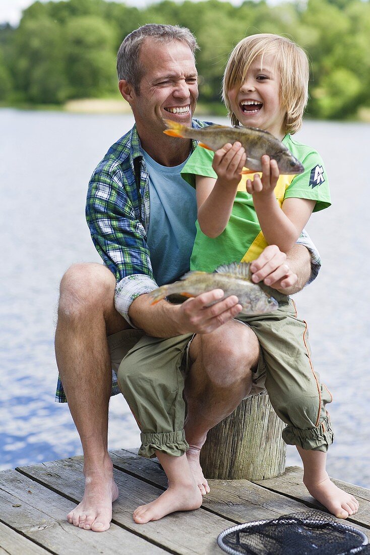 Vater und Sohn mit frisch gefangenen Fischen am Bootssteg