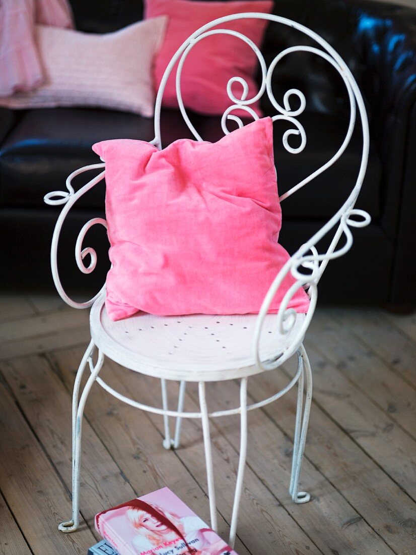 A pink cushion on a white metal chair