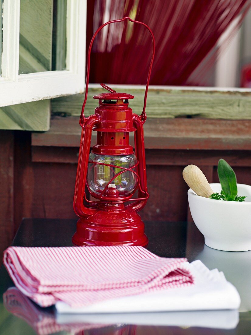 An oil lamp, a mortar and dish cloths in front of an open window