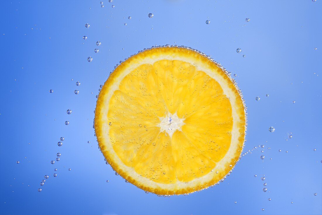 Orangenscheibe im blauen Wasser mit Luftbläschen