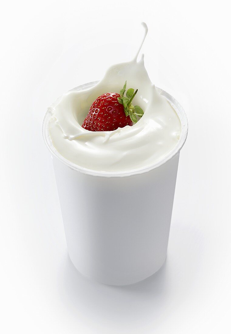 A strawberry falling into a cup of yogurt