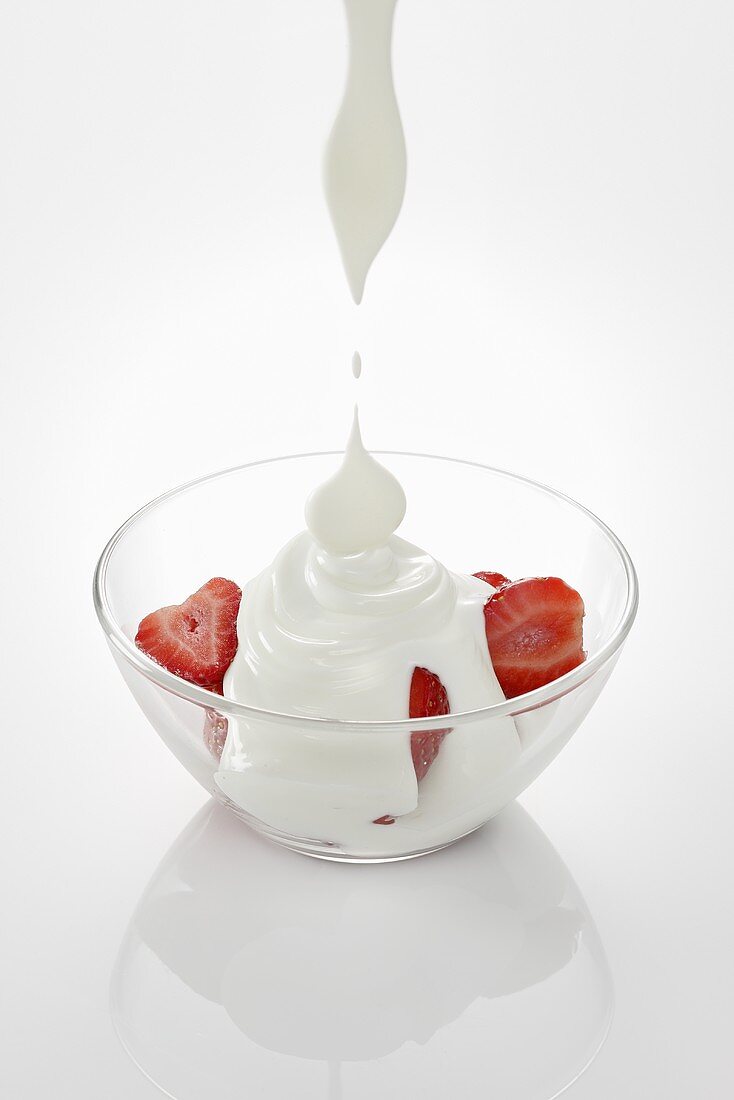 Joghurt tropft auf Erdbeeren in Glasschale
