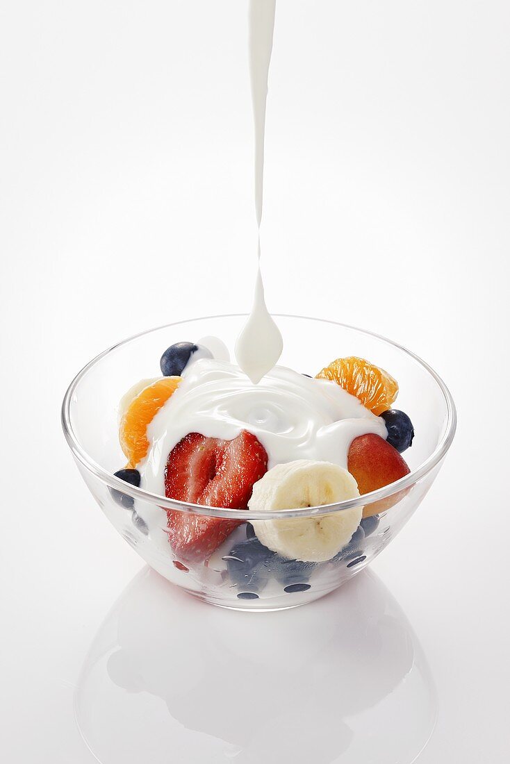 Yogurt being poured onto fruit in a glass bowl