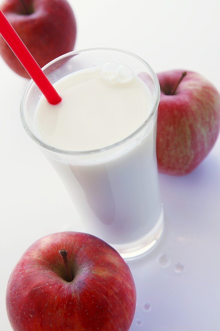 Milchglas mit Strohhalm und drei rote Äpfel