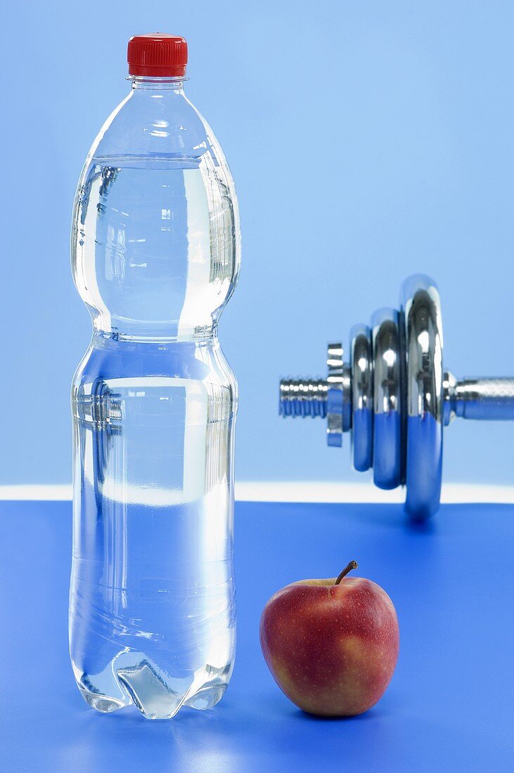 A bottle of mineral water, an apple and a dumbbell