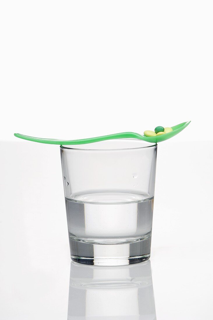 Löffel mit Vitaminpillen auf Wasserglas