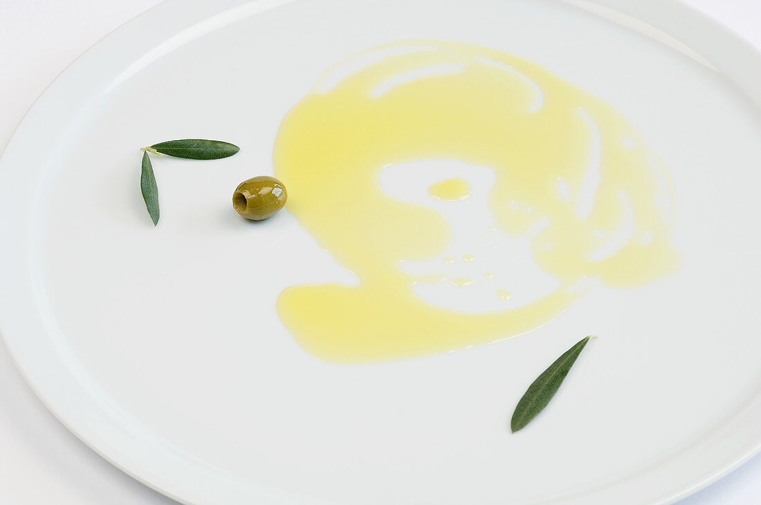 Olive oil, green olives and olive leaves on a plate