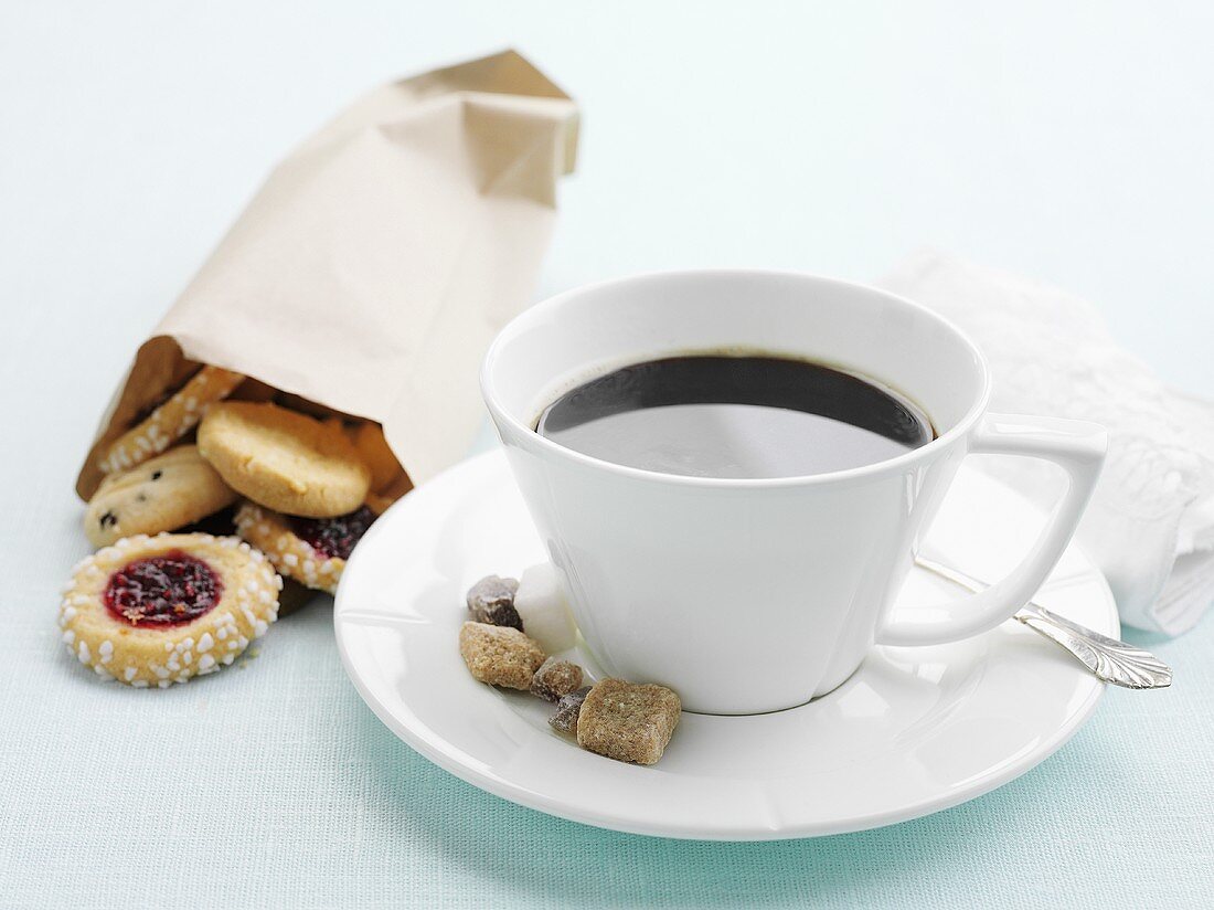 A cup of coffee with sugar and a bag of biscuits