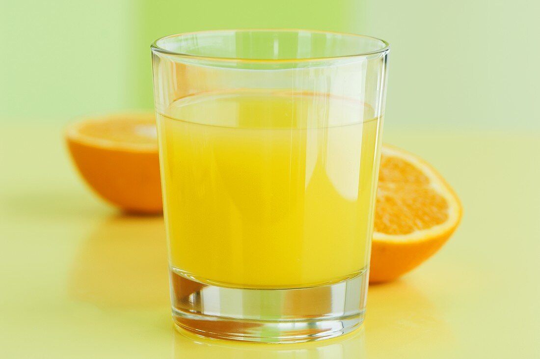 A glass of orange juice with orange halves behind it