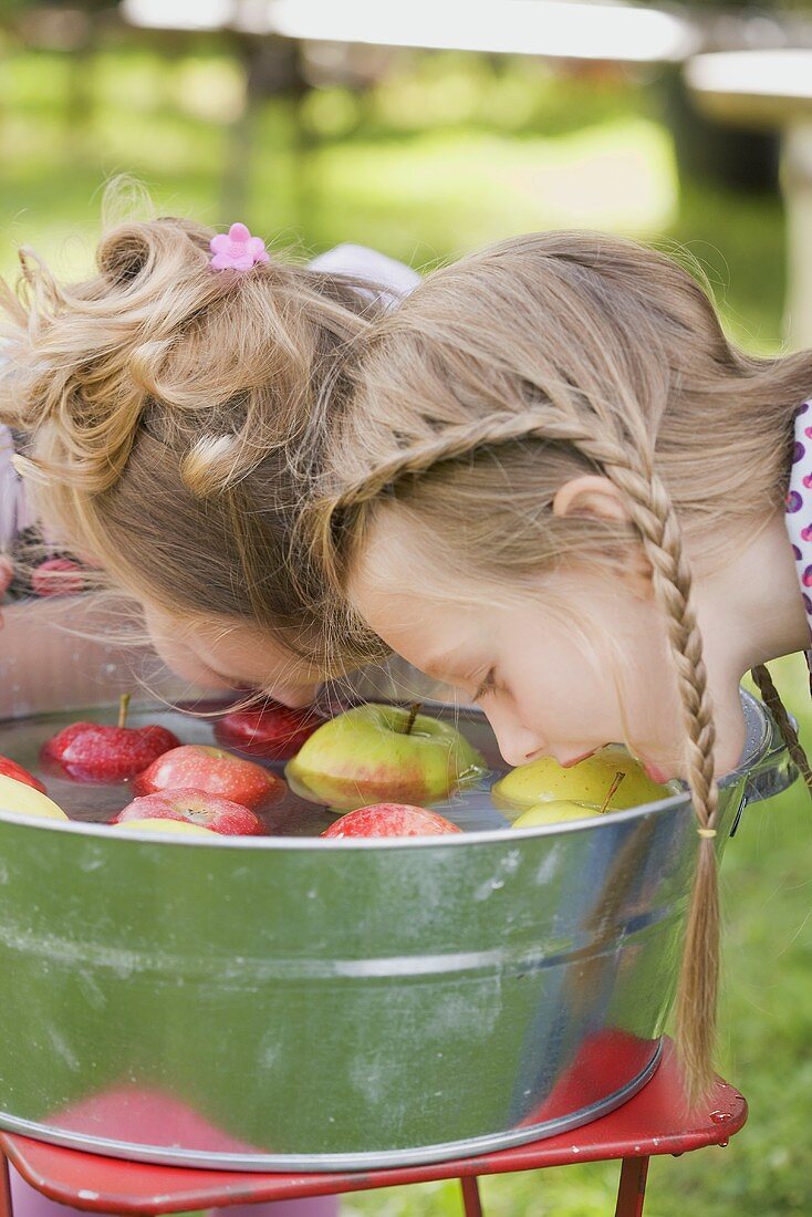 Two girls bobbing for apples