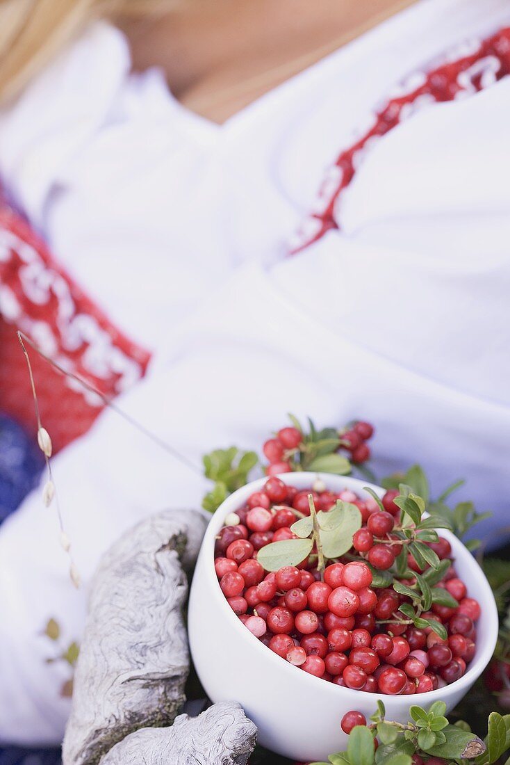 A bowl of fresh lingonberries with a woman in the background