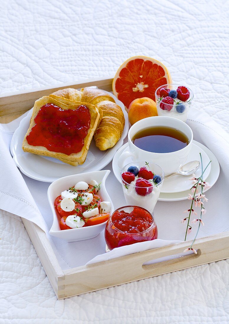 Breakfast in bed with tea, jam, yogurt, fruit and tomatoes and mozzarella