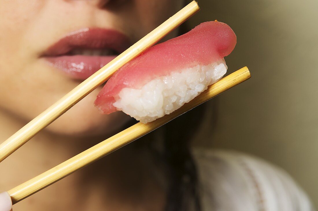 A woman holding a nigiri sushi chopsticks