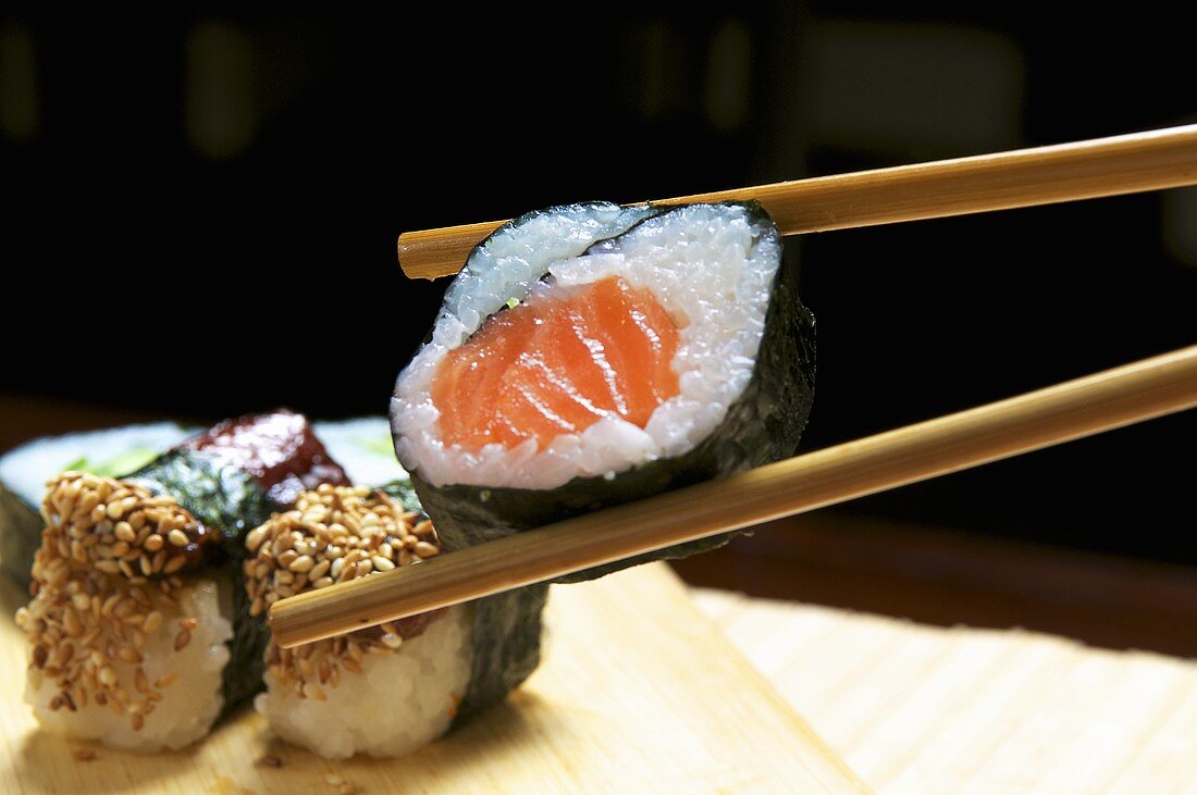 Maki-Sushi mit Lachs zwischen Essstäbchen