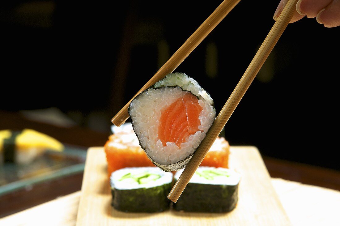 Hand hält Essstäbchen mit Maki-Sushi