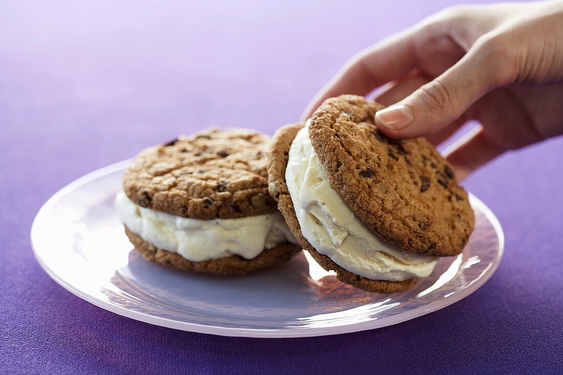 Hand Grabbing a Cookie Ice Cream Sandwich From a Plate