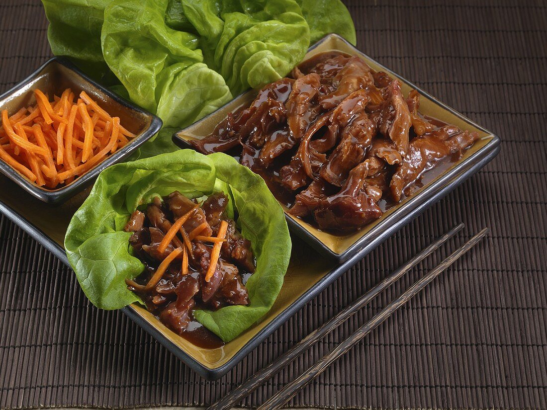 Schweinefleisch asiatisch zubereitet, mit Möhrenstreifen auf Salatblatt
