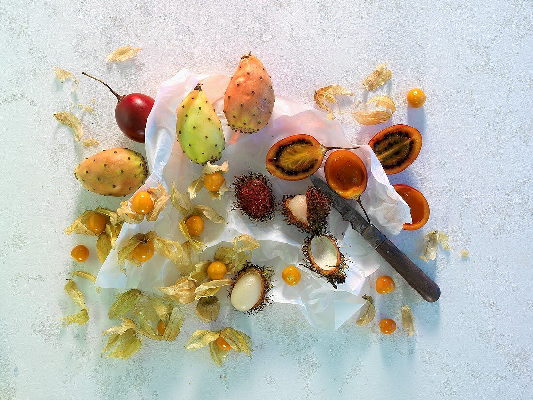 Tunas, tamarillos, lychees and star fruit on paper with a knife