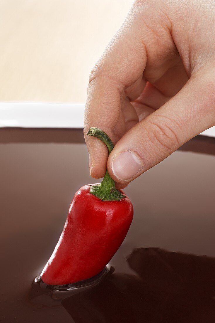Hand dippt rote Chilischote in Schokoladensauce